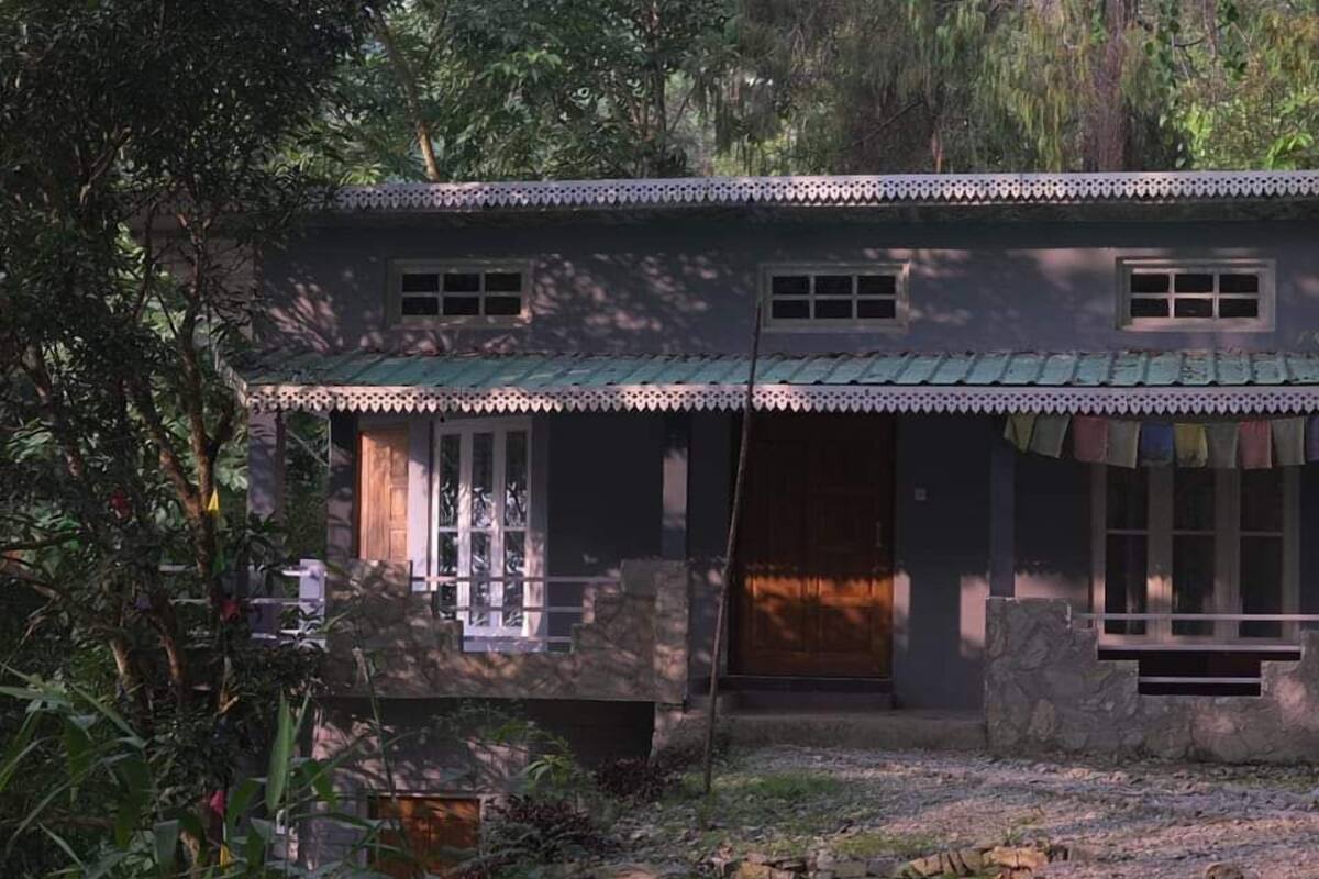 A two-story house with a porch, stone walls, and a green roof.