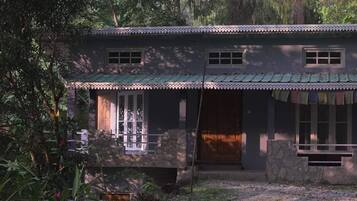 A two-story house with a porch, stone walls, and a green roof.