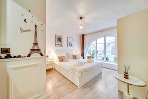 A bedroom with a large bed, a small table, and a window with a view. - Résidence Paris CHOISEUL (Paris)