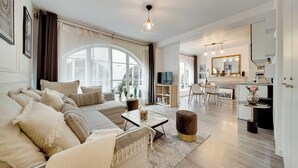 Un'ampia zona giorno con divano, tavolino e poggiapiedi, un'area pranzo con tavolo e sedie, e una cucina con specchio e piano di lavoro.
