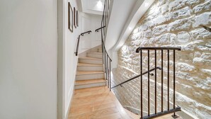 Una scala con gradini in legno, pareti bianche e una parete in pietra alla destra.