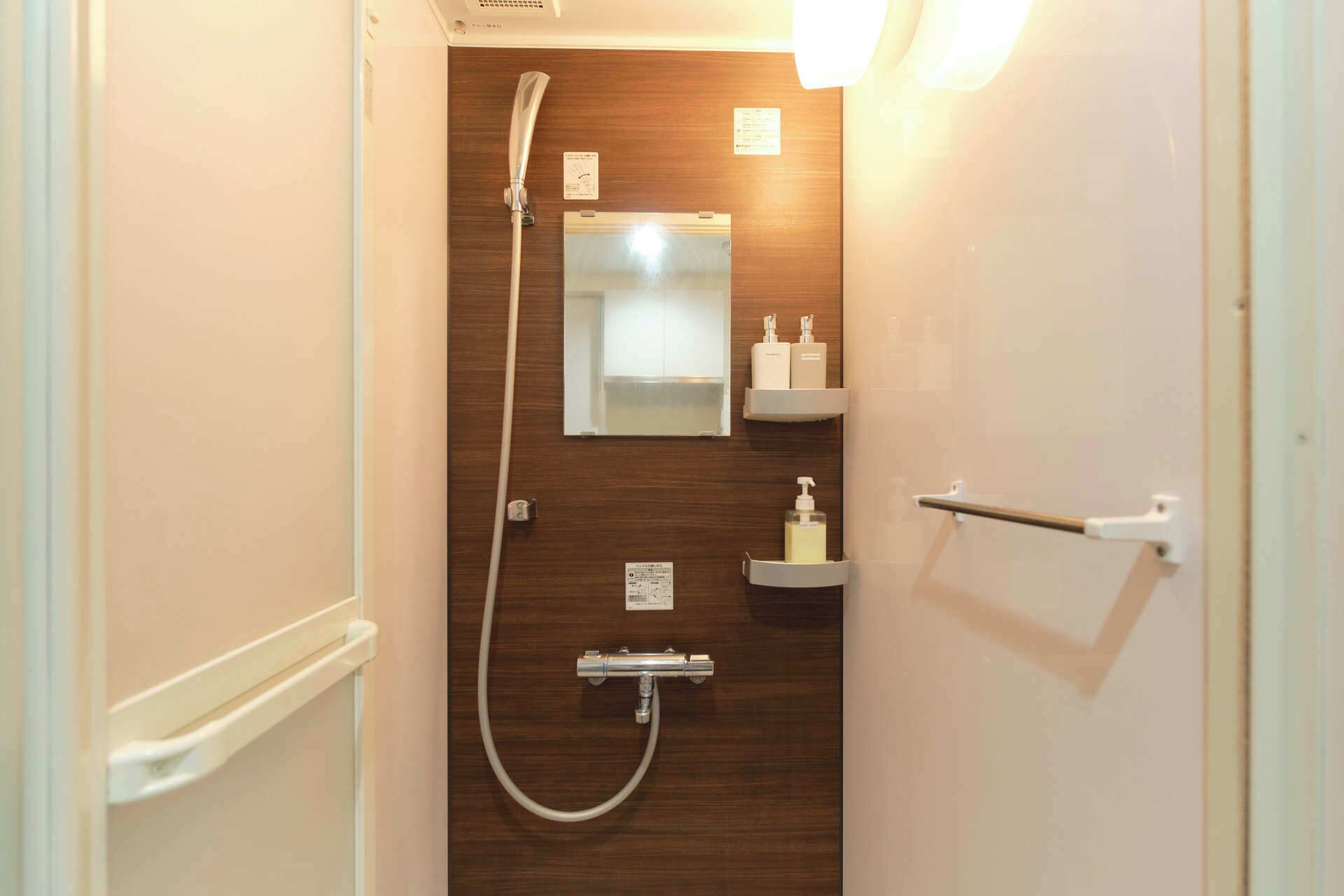 A bathroom with a shower, a mirror, and two shelves with toiletries.