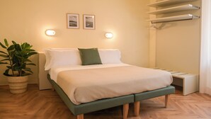 A neatly arranged bedroom with a bed, bedside tables, a potted plant, and wall-mounted lights.