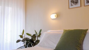 Quarto de hotel com uma cama, um travesseiro verde, uma luminária fixada na parede e duas imagens emolduradas.