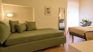 Um quarto com um sofá verde, uma cama, uma mesinha e um espelho.