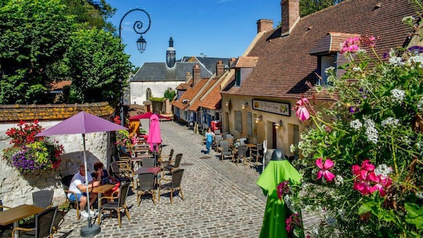 Eine Kopfsteinpflasterstraße gesäumt von traditionellen Gebäuden, mit Außenplätzen und blauem Himmel.