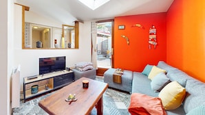 Ein modernes Wohnzimmer mit großem Fernseher, einem Holztisch und einer Couch mit bunten Kissen.