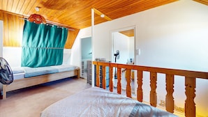 Ein Schlafzimmer mit Holzboden, einem Bett, einem kleinen Schreibtisch, einem Spiegel und einem Fenster mit Vorhängen.