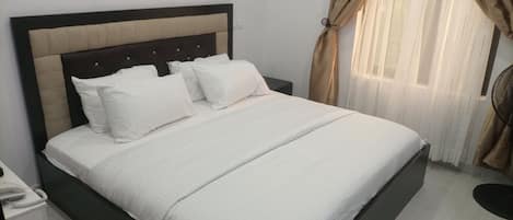 A neatly made bed with white bedding and a dark headboard, a bedside telephone, and a window with curtains.