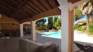 En udendørs patio med pool, fletmøbler og en pergola.