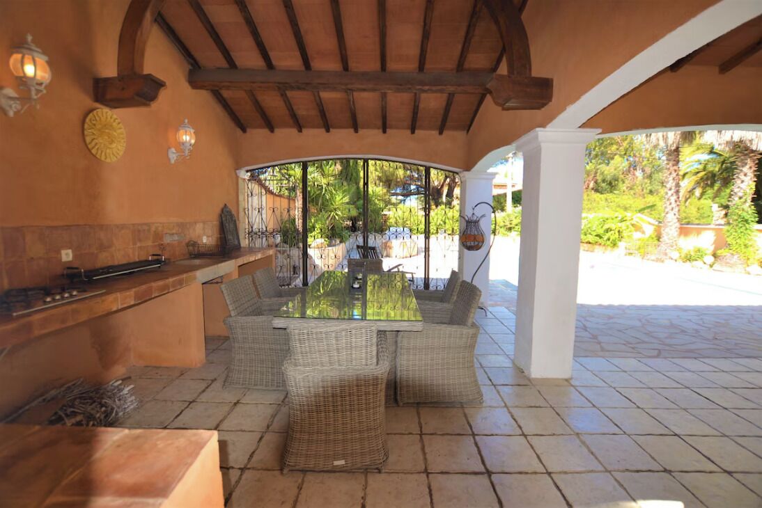 Une terrasse extérieure aménagée avec des meubles en osier, une table à plateau en verre et un bar intégré.