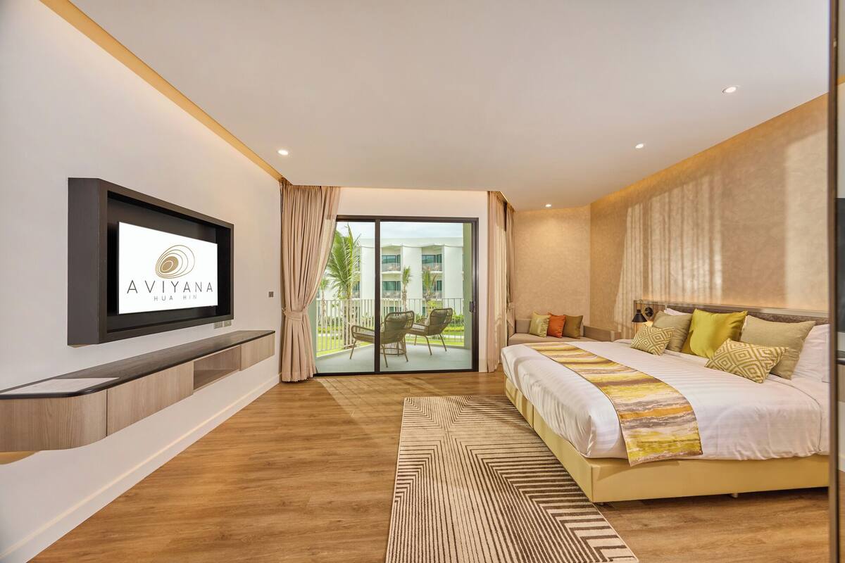 Una habitación de hotel moderna con una cama grande, un televisor montado en la pared y un ventanal corredero que da a un balcón.