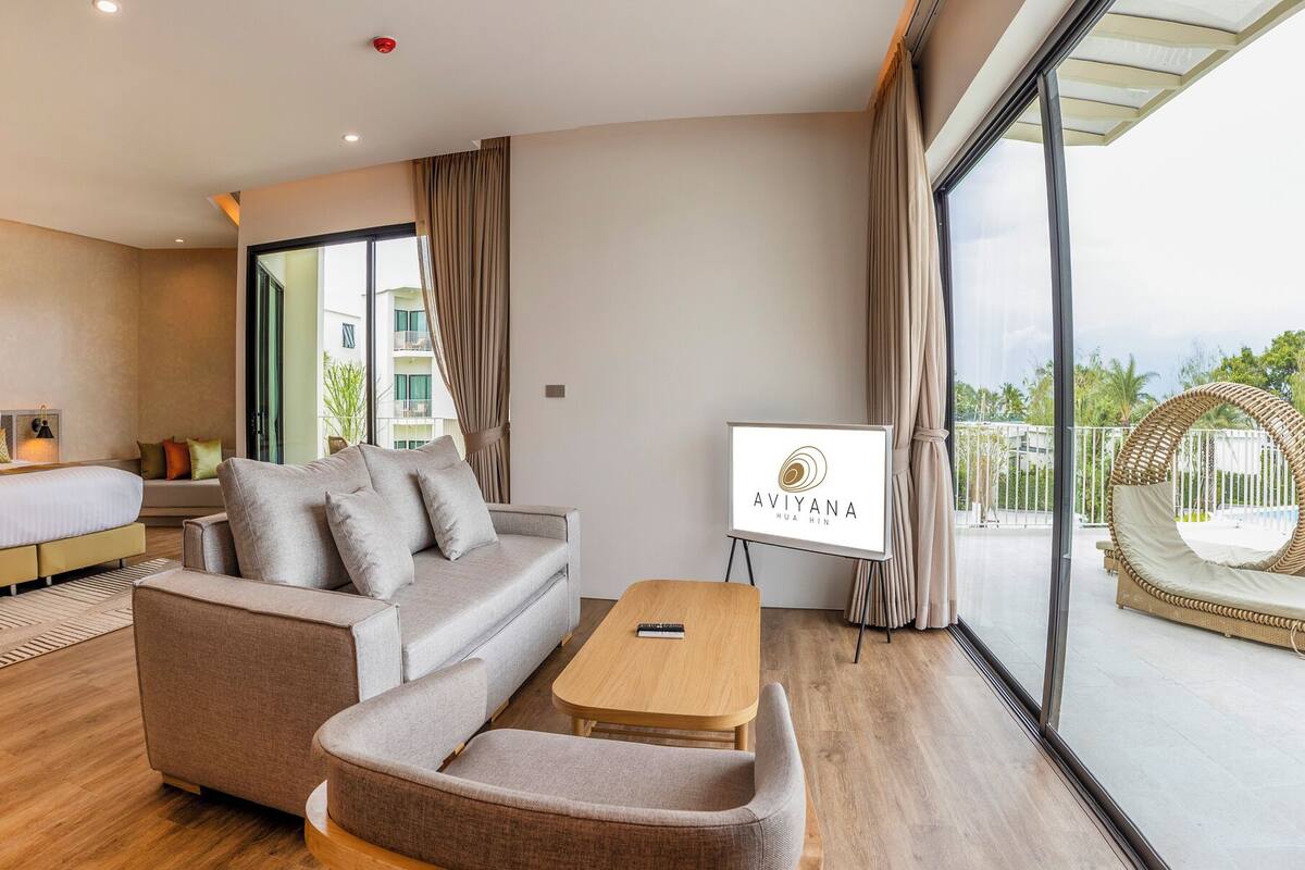 Una habitación de hotel moderna con sofá, cama, mesa de centro de madera y vistas al exterior.