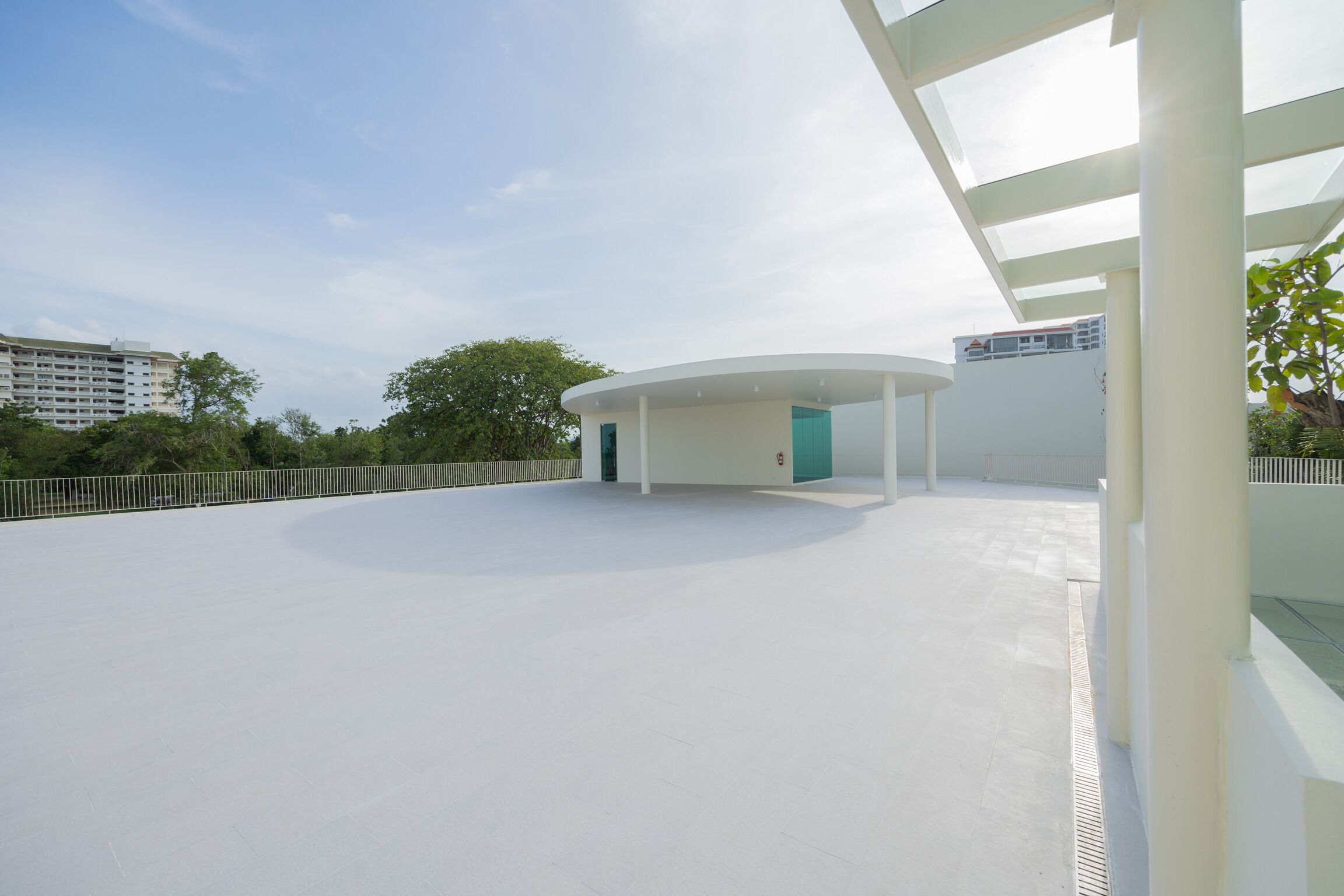 Un espacio exterior amplio y moderno con una estructura circular y techo plano, rodeado de vegetación y un cielo despejado.