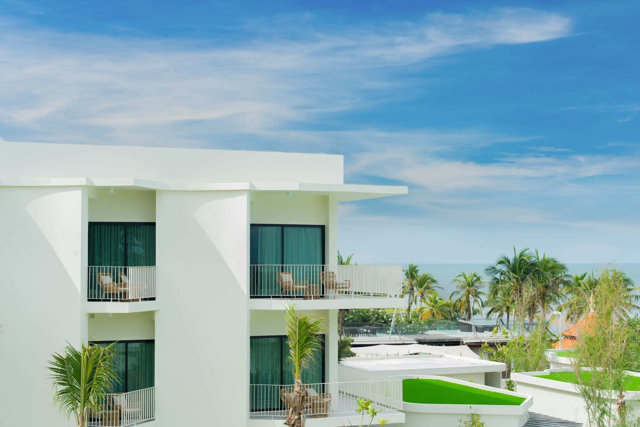 A modern multi-story hotel with balconies, a pool area, and views of the ocean.