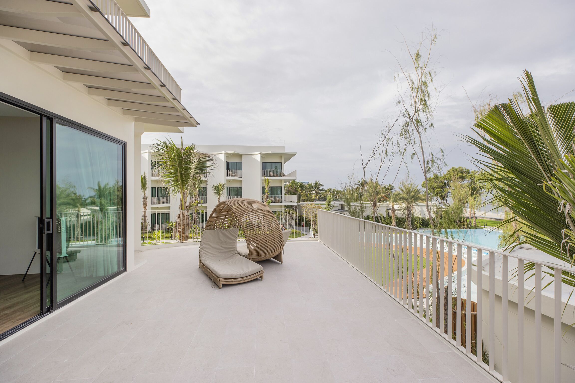 Ein Balkon mit Glastür, Liegestuhl und Pool im Hintergrund.