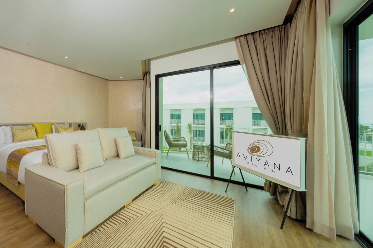 Habitación de hotel con cama, sofá, ventana grande y vista al edificio.