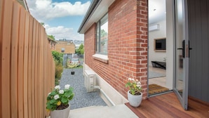 Et moderne hus med murstensfacade, et træhegn og en grussti, der fører til en dør.