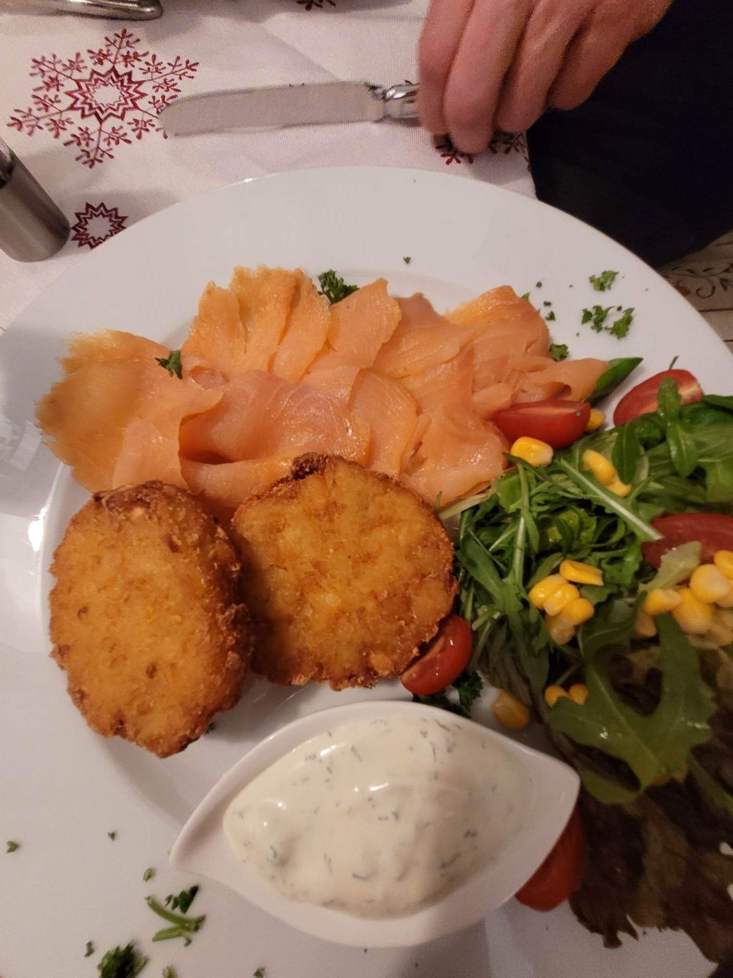 A plate with smoked salmon, fried items, a salad, and a creamy sauce.