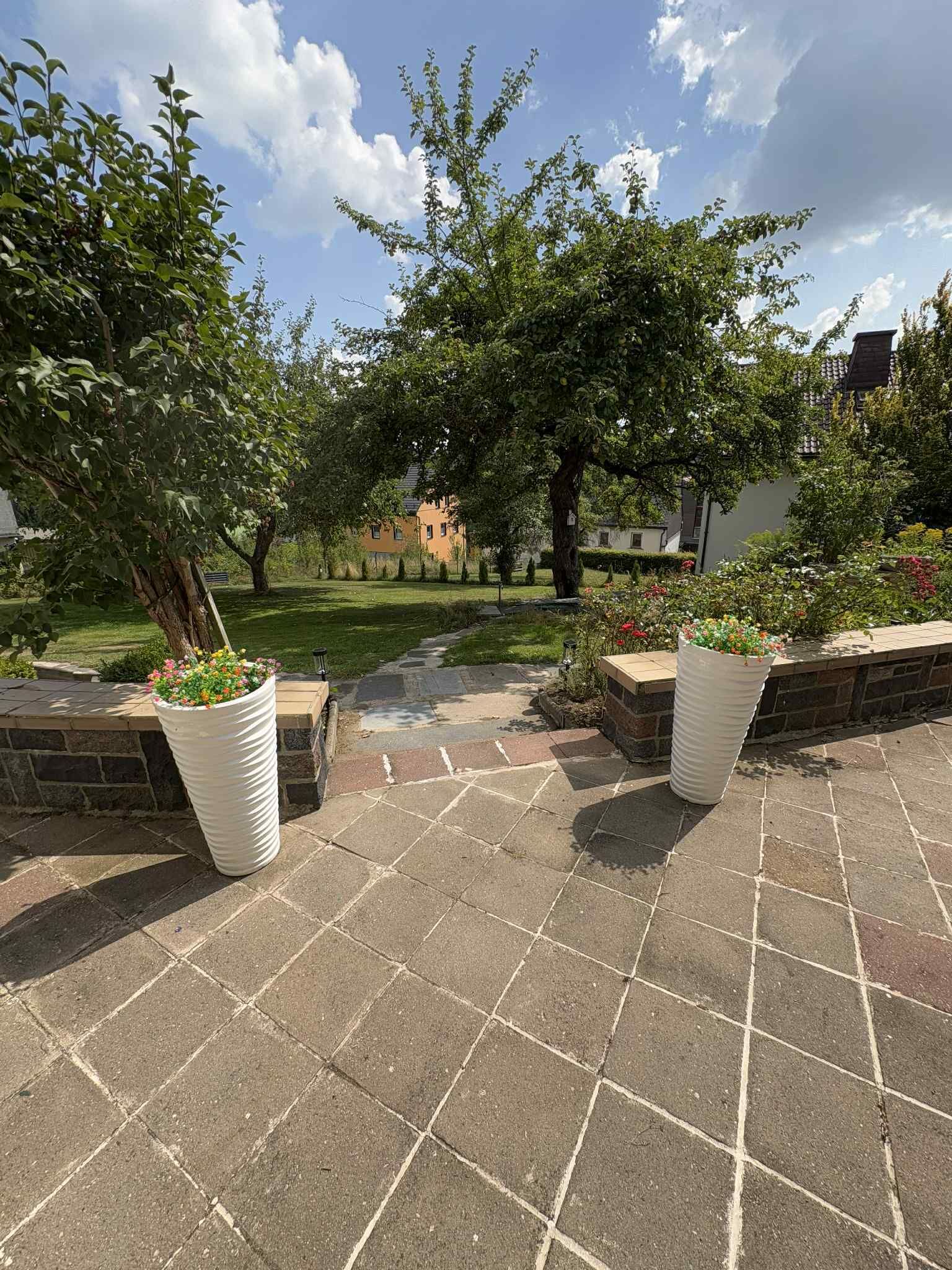 Une terrasse dallée, agrémentée de grands jardinières et d’une pelouse en arrière-plan.