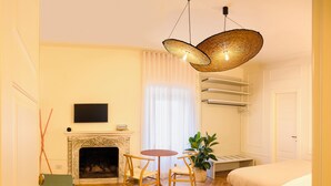 A room with a fireplace, a round table with chairs, a bed, a hanging light fixture, and a potted plant.