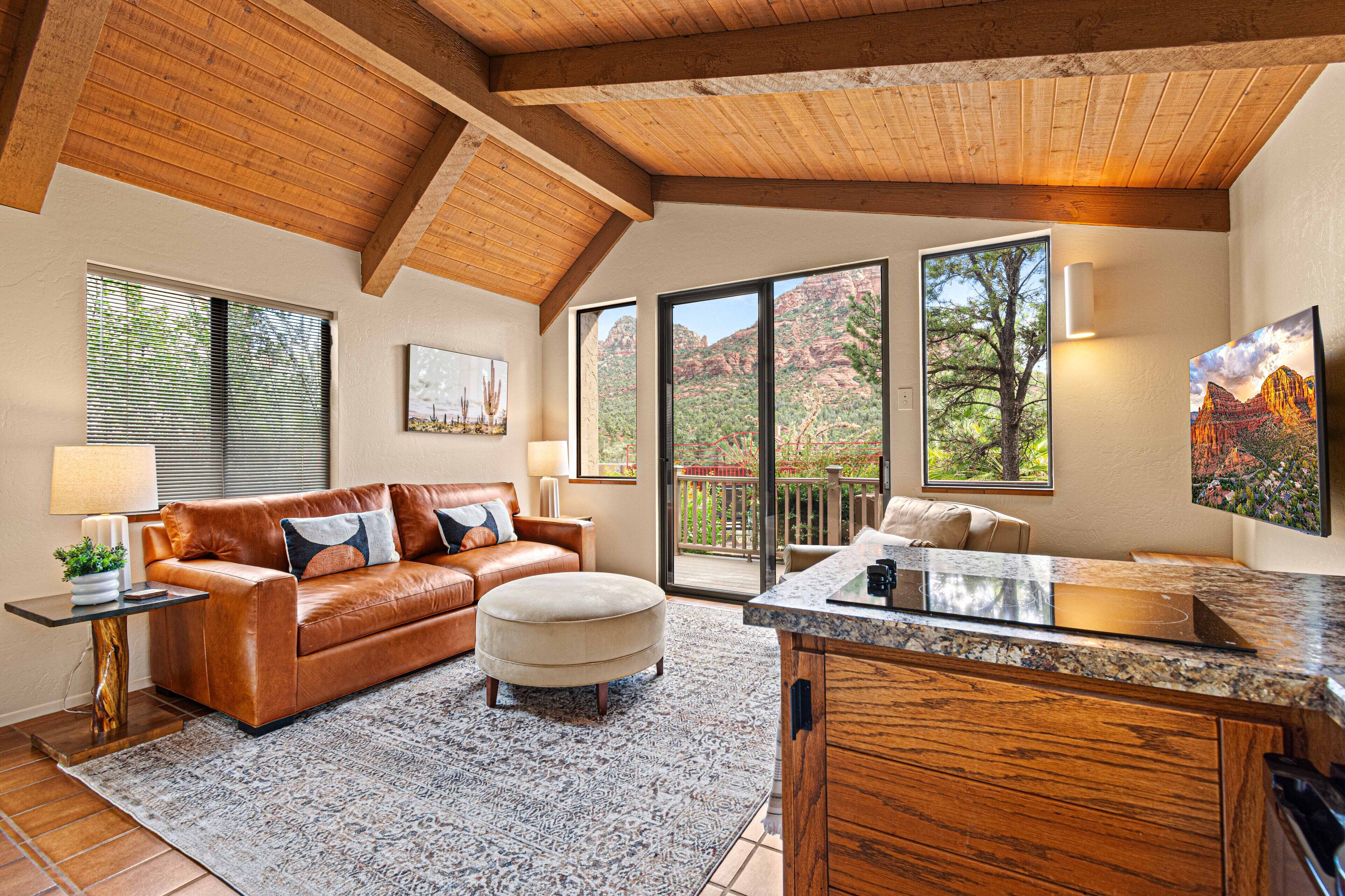 A spacious living room with a leather sofa, ottoman, and a large window offering a view of the outdoors.
