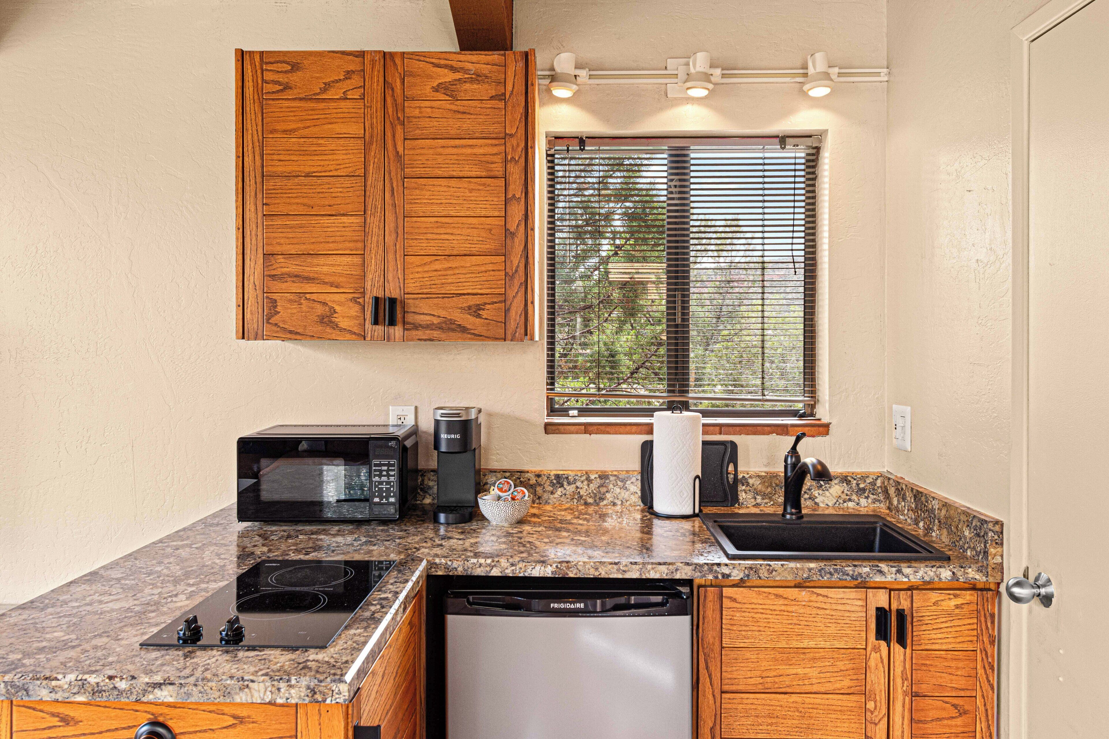 A compact kitchen with wooden cabinets, a built-in microwave, a coffee maker, a sink, and a dishwasher.