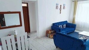 A living room with a blue sofa, a white chair, a small table, and a door leading to another room. - Lux Suites Lakira Shades Ongata Rongai (Ongata Rongai)