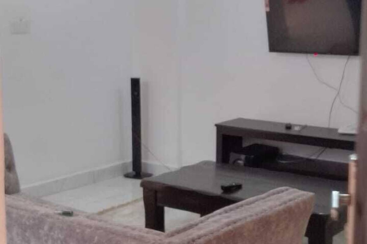 A living room with a sofa, a coffee table, a TV, and a flat-screen TV mounted on the wall.