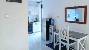 A compact kitchen with white cabinets, a refrigerator, and a dining table with chairs. - Lux Suites Lakira Shades Ongata Rongai (Ongata Rongai)