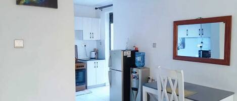 A compact kitchen with white cabinets, a refrigerator, and a dining table with chairs.