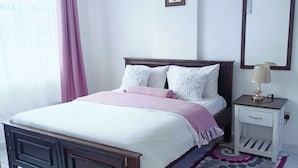 A bedroom with a bed, bedside table, and a mirror. - Lux Suites Lakira Shades Ongata Rongai (Ongata Rongai)