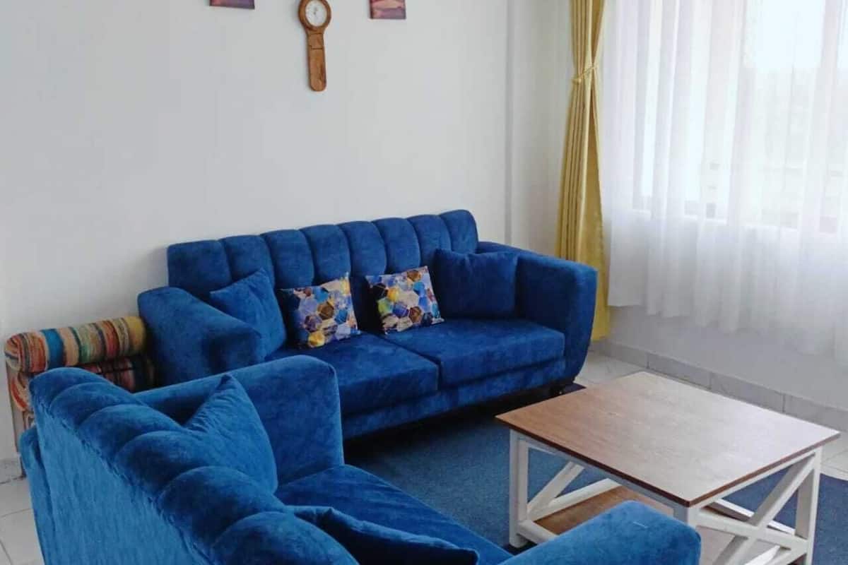 A living room with a blue sofa set, a wooden coffee table, and a colorful throw pillow.