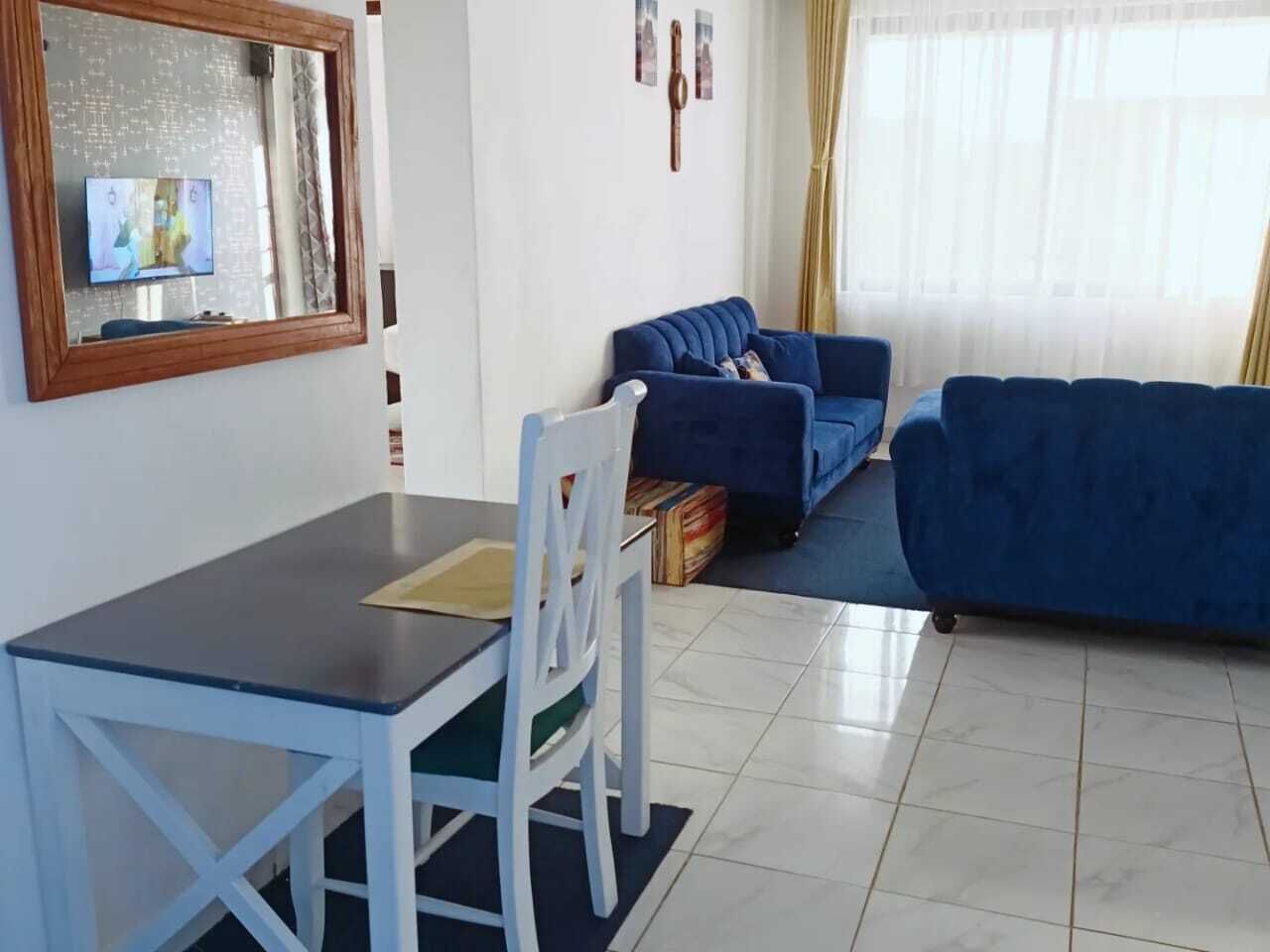 A living room with a blue sofa, a dining table with chairs, and a television on the wall.