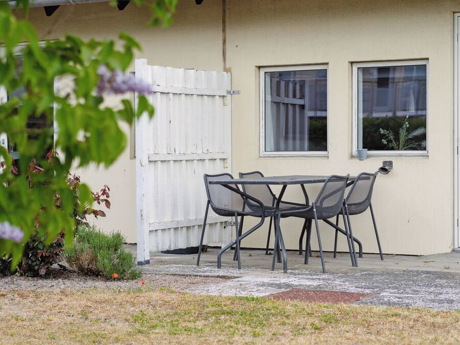 Un patio con una mesa y sillas, un cerco blanco y un edificio con dos ventanas.