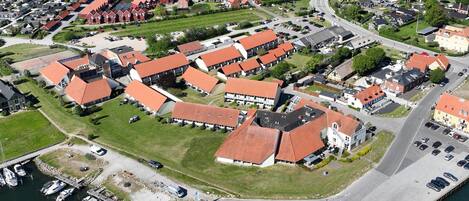 Vista aérea de una zona residencial con casas de techo rojo, un puerto deportivo con barcos y una carretera serpenteando por el vecindario.