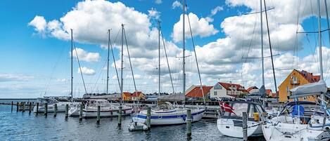 A marina with multiple sailboats docked at wooden piers, surrounded by buildings with red and yellow roofs.