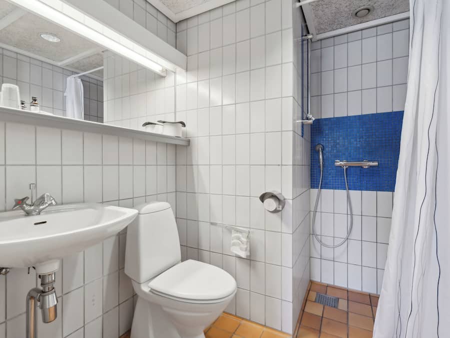 Un baño con lavamanos, inodoro y ducha blancos.