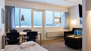 Une chambre d’hôtel comprenant un lit, un bureau avec des chaises, un canapé et de grandes fenêtres donnant sur un paysage.