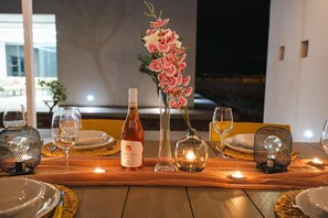 Una mesa dispuesta para comer, con botellas de vino, copas y un florero con flores.