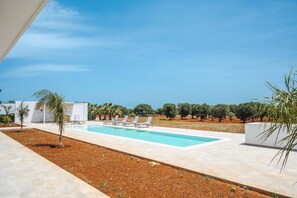 Un área de piscina moderna al aire libre con sillones de descanso y vistas a olivos.