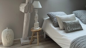 A bedroom with a sloped ceiling, a skylight, a bed with grey bedding, a white lamp, and a decorative vase.