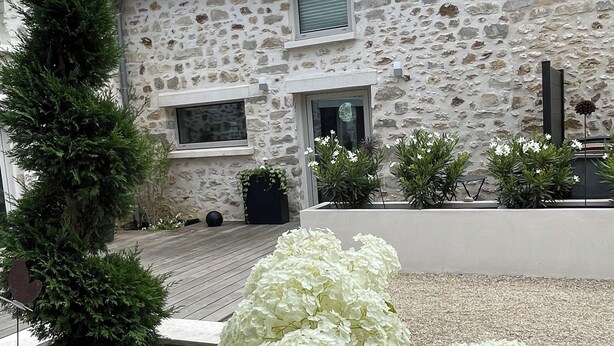 A stone building with a tiled roof, a wooden deck, and white hydrangea plants in the foreground.