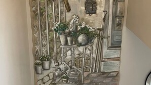 A wall-mounted artwork depicting a rustic outdoor scene with plants and a lantern.