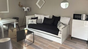 A modern living room with a white sofa, a small table, a chair, a floor lamp, and a microwave.