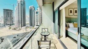A balcony with a view of high-rise buildings, a glass table, and a bed with a view. - Cosmos Living - Goldcrest Views1  (Dubai)