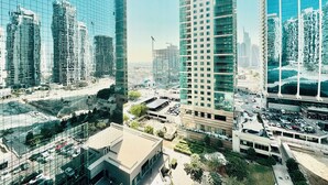 A high-rise building with a glass facade, surrounded by other tall buildings and a busy street with cars. - Cosmos Living - Goldcrest Views1  (Dubai)