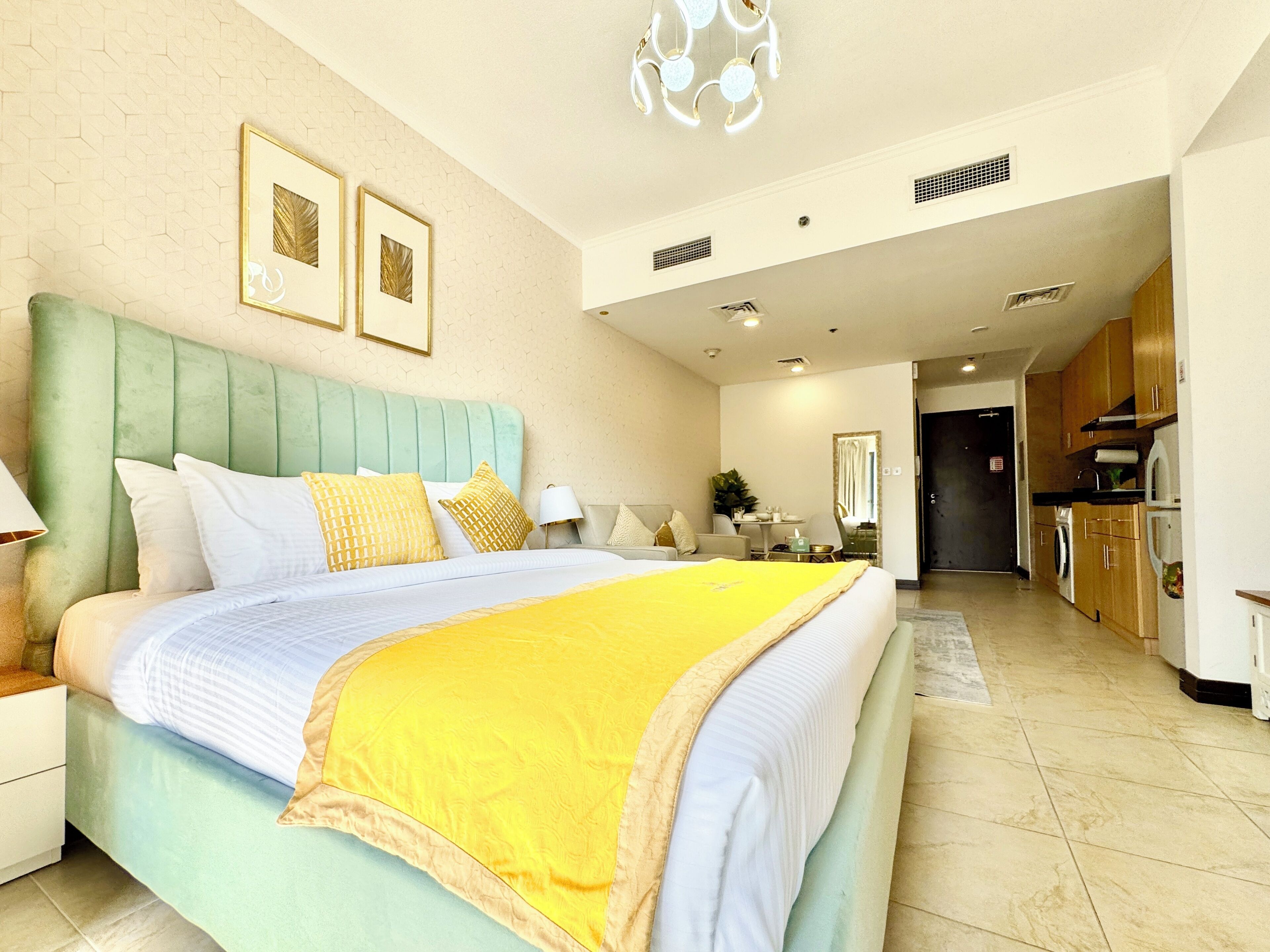 Quarto de hotel moderno com uma cama grande, uma kitchenette e um banheiro visível através de uma porta aberta.