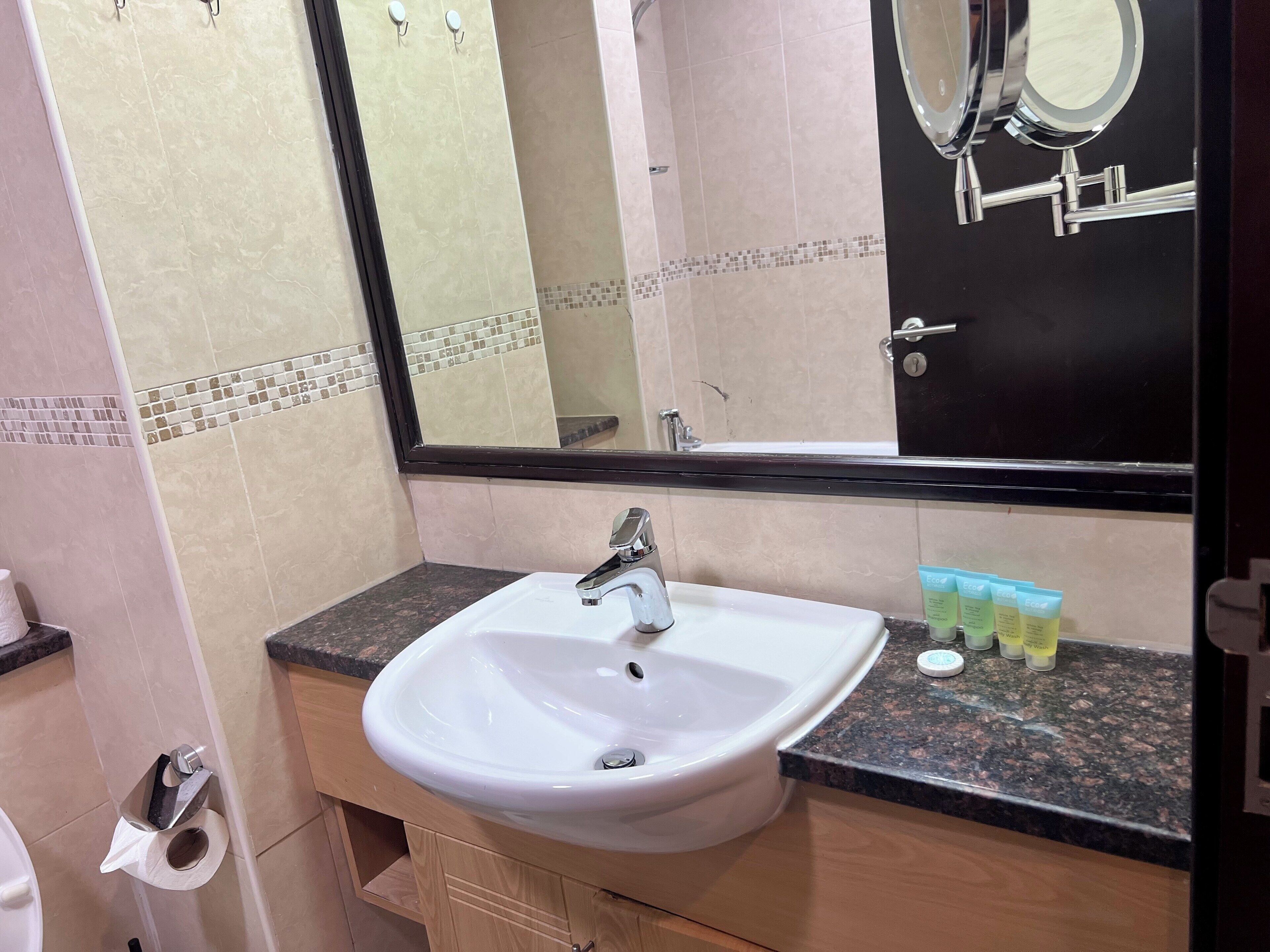 A bathroom with a white sink, a mirror, and toiletries on the countertop.