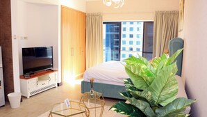A modern hotel room with a large bed, a flat-screen TV, a glass coffee table, and a large plant. - Cosmos Living - Goldcrest Views1  (Dubai)